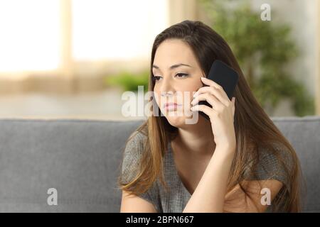 Femme ennuyés pendant un appel téléphonique assis sur un canapé dans le salon dans une maison avec un contexte intérieur Banque D'Images