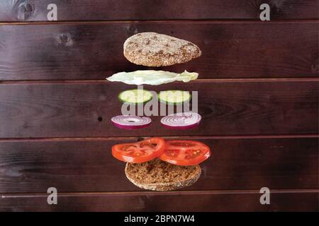 Vue rapprochée d'un sandwich maison avec des ingrédients volants sur fond de bois. Banque D'Images