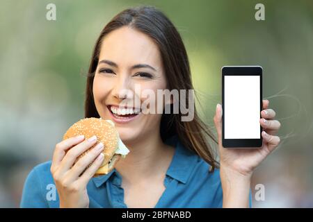 Happy woman holding a hamburger montrant un écran de téléphone dans la rue Banque D'Images