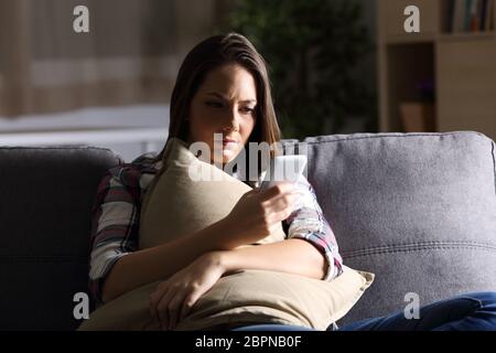 Sad girl holding oreiller et lecture du message téléphonique dans le noir assis sur un canapé à la maison Banque D'Images