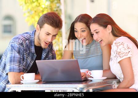 Trois amis surpris à regarder en ligne des contenus médias sur ordinateur portable dans un café Banque D'Images