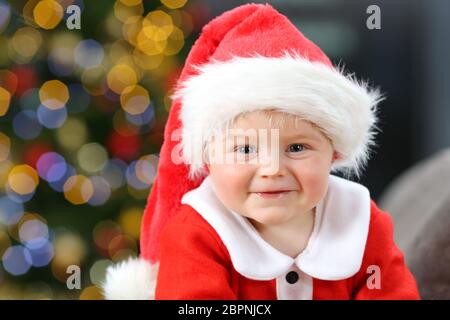 Happy kid wearing santa claus dress looking at camera sur un canapé à la maison à Noël Banque D'Images