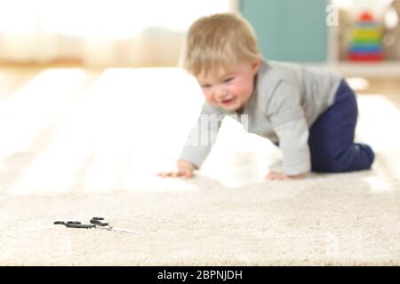 Bébé en danger rampant vers un ciseaux sur un tapis à la maison Banque D'Images