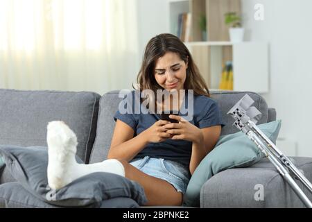 Triste mobilité girl texting on phone assis sur un canapé dans la salle de séjour à la maison Banque D'Images