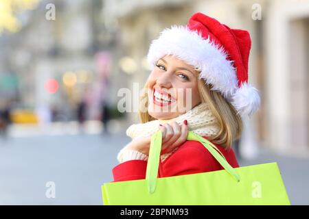 Portrait d'une femme heureuse weating a santa claus hat shopping de Noël en vous regardant à l'extérieur sur la rue Banque D'Images