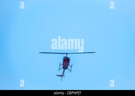 Un petit hélicoptère commercial à deux places placé contre un ciel bleu clair passe de bas en haut. Un petit hélicoptère vole dans un ciel bleu clair. Banque D'Images