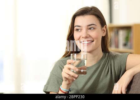 Titulaire d'un des ados distraits en verre à côté de l'eau assis sur un canapé dans la salle de séjour à la maison Banque D'Images