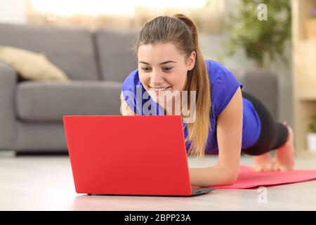 Fitness petite fille l'exercice de regarder en ligne des vidéos dans un ordinateur portable rouge se trouvant sur le plancher dans la salle de séjour à la maison Banque D'Images