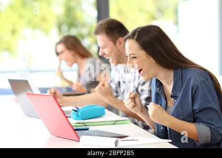 Trois camarades excités de recevoir de bonnes nouvelles en ligne dans leurs ordinateurs portables dans une salle de classe Banque D'Images