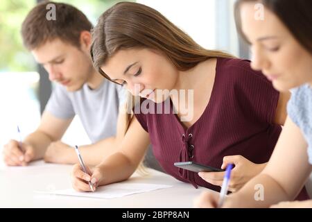 Étudiant en utilisant un téléphone intelligent à copier lors d'un examen dans une salle de classe Banque D'Images