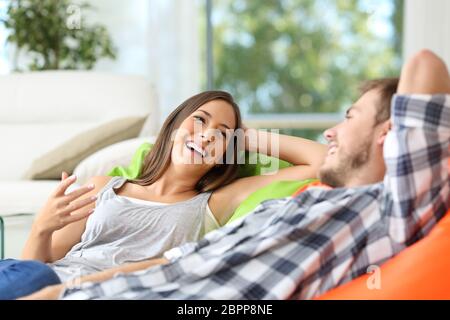 Couple ou colocataires parler et rire couché sur poufs dans la salle de séjour à la maison avec une fenêtre à l'arrière-plan Banque D'Images
