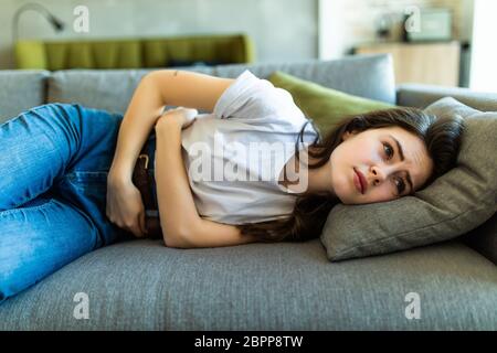 Portrait de jeune femme souffrant de mal de ventre sur canapé à la maison Banque D'Images