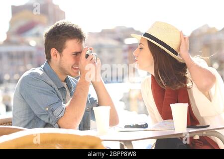 Vue latérale d'un touriste de plaisanter et de photographier sa petite amie dans une terrasse de l'hôtel pendant les vacances Banque D'Images