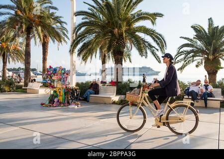 Une jeune femme à la mode fait du vélo le long de la promenade Riva, Split, Croatie Banque D'Images