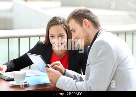 Deux cadres consultant des données en ligne sur une tablette, assis sur une terrasse de restaurant Banque D'Images