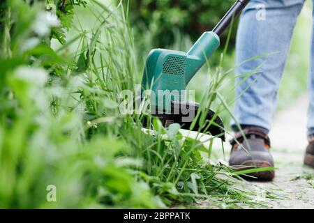 Homme tond l'herbe haute avec un coupe-herbe électrique. Concept de soin de cour Banque D'Images