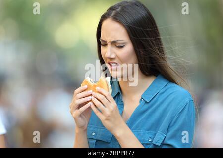 Dégoûté femme manger un burger avec de mauvais goût sur la rue Banque D'Images