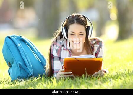 Vue avant portrait d'un étudiant à lire des notes et d'écouter un tutoriel audio à la ligne allongée sur l'herbe dans un parc Banque D'Images