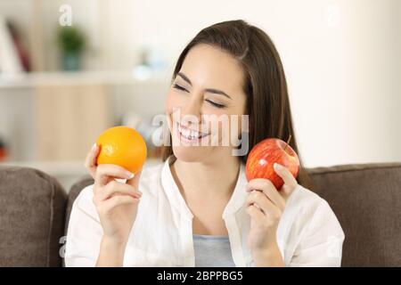 Happy woman décider entre différents fruits assis sur un canapé dans la salle de séjour à la maison Banque D'Images