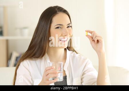 Heureux dame holding et montrant une vitamine comprimé et un verre d'eau à la maison Banque D'Images