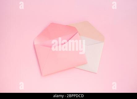Deux enveloppes en papier rose et blanc sur fond rose pastel. Banque D'Images