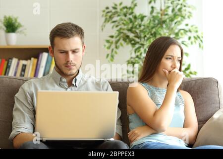 Mari utilisant un ordinateur portable en ligne ignorant à sa triste femme assis sur un canapé à la maison Banque D'Images