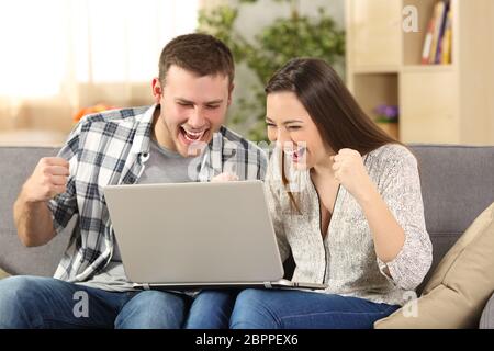 Heureux couple reading nouvelles en ligne assis sur un canapé dans la salle de séjour à la maison Banque D'Images