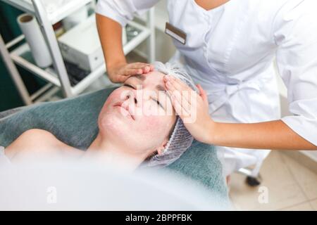 Le médecin esthéticienne fait un massage cosmétique du visage. Une femme se détend sur une chaise cosmétique Banque D'Images