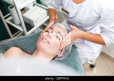 Le médecin esthéticienne fait un massage cosmétique du visage. Une femme se détend sur une chaise cosmétique Banque D'Images