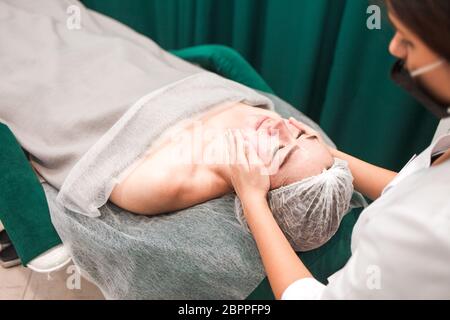 Le médecin esthéticienne fait un massage cosmétique du visage. Une femme se détend sur une chaise cosmétique Banque D'Images