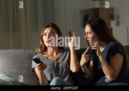 Femme en colère montrant téléphone et ami l'ignorant assis sur un canapé dans la salle de séjour à la maison Banque D'Images