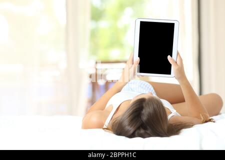 Full body portrait d'une jeune fille étendue sur le lit regardant et montrant un écran tablette vierge Banque D'Images