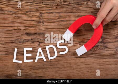 Person's Hand Holding Horseshoe aimant qui attire conduit blanc lettre sur fond de bois Banque D'Images
