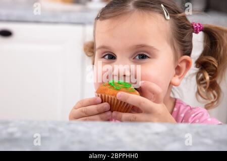 Portrait Of Happy Girl having fun while eating Cupcake savoureux dans la cuisine Banque D'Images