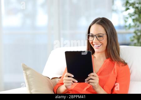 Casual woman wearing glasses reading une tablette assise sur un sofa à la maison avec une fenêtre à l'arrière-plan Banque D'Images