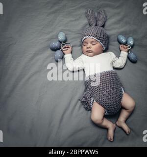 Mignon petit bébé habillé comme un lapin de Pâques, adorable Enfant dormir sur la couverture grise avec arrière-plan gris élégant décoré des oeufs de Pâques, heureux rel Banque D'Images