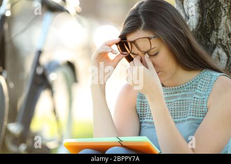 Seul élève souffrant de fatigue visuelle tout en portant des lunettes est étudiant dans un parc Banque D'Images