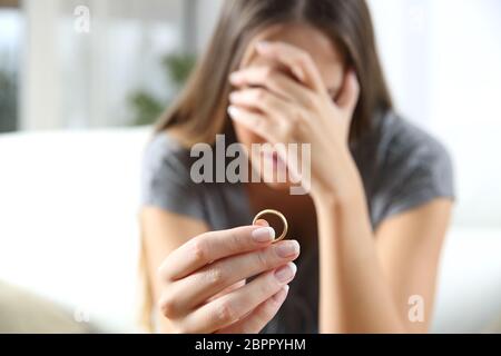 Libre d'une seule femme triste après divorce déplorant holding l'anneau de mariage dans une house interior Banque D'Images