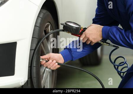 Close up d'un mécanicien de voiture mains contrôle de l'air des pneus avec un manomètre Banque D'Images