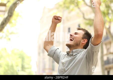 Portrait d'un homme excité raising arms dans la rue avec des bâtiments en arrière-plan Banque D'Images