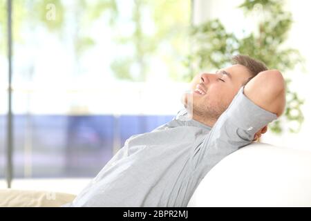 Vue latérale d'un heureux homme attrayant se reposant et respirant assis sur un canapé à la maison avec une fenêtre avec un fond vert à l'extérieur Banque D'Images