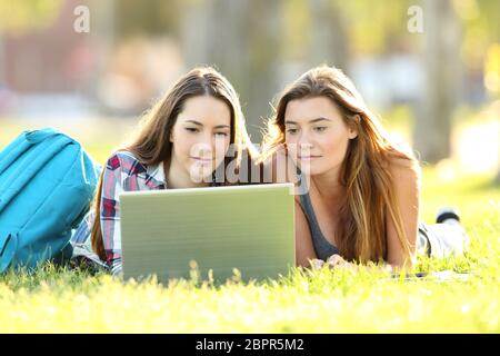 Vue de face de deux élèves, l'apprentissage en ligne avec coffre allongé sur l'herbe dans un campus universitaire Banque D'Images