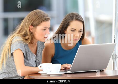 Deux amis sérieux regardant du contenu multimédia dans un ordinateur portable en ligne assis dans un bar Banque D'Images