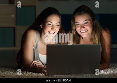 Deux adolescents regardant sur la ligne du contenu dans un ordinateur portable se trouvant sur le plancher dans une chambre dans la maison avec une lumière sombre dans l'arrière-plan Banque D'Images