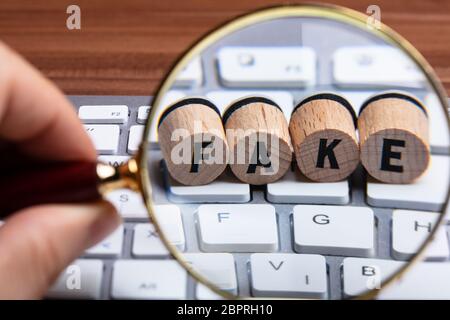 Man's Hand Holding Loupe sur liège en bois avec de faux texte sur clavier blanc Banque D'Images