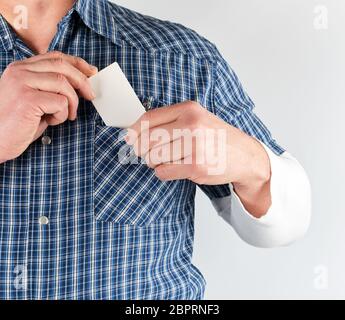 L'homme en chemise bleue met dans sa poche une carte papier blanc vide, fond blanc Banque D'Images