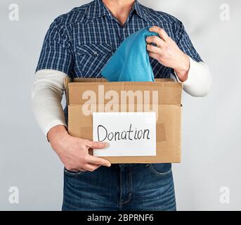 L'homme dans une chemise à carreaux bleu jeans et détient une grande boîte de papier brun avec l'inscription don, concept de l'aide aux nécessiteux, fond blanc Banque D'Images