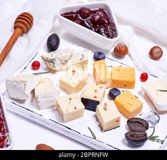 De petits morceaux de fromage brie, roquefort, camembert, cheddar et fromage aux noix sur une planche de bois blanc, vue du dessus Banque D'Images