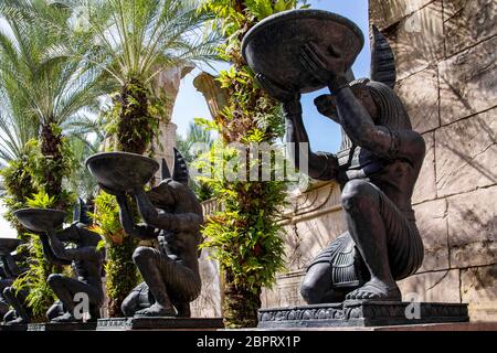 Alley avec de grandes statues en pierre identiques du dieu égyptien Anubis, qui se dresse sur un genou et est titulaire d'une cuvette ronde dans ses mains. Palms croître entre e Banque D'Images