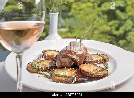 Rôti de porc glacé aux pommes de terre sautées et aux épices fraîches servi dans une assiette blanche sur une table de restaurant. Banque D'Images